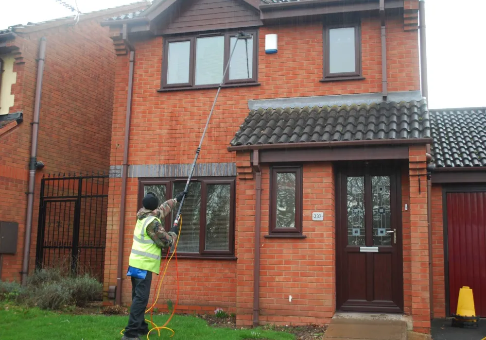 Window cleaner cleaning the upstairs windows of a red-brick house with a water-fed pole