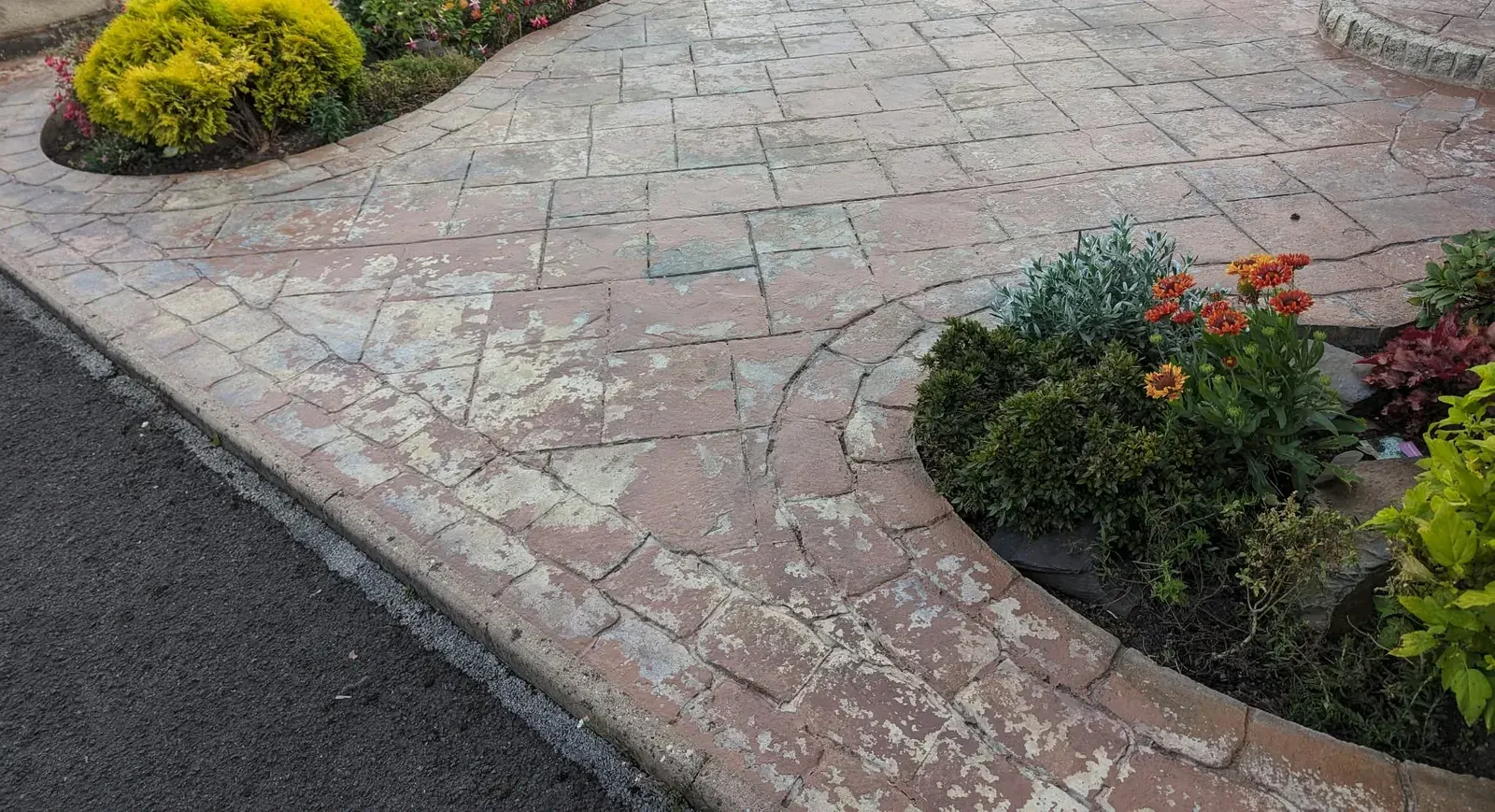 Faded imprinted concrete driveway around a flower bed before resealing